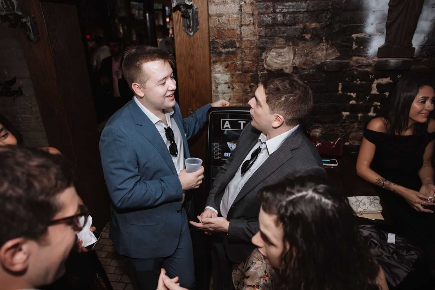 Two men in suits having conversation at wedding reception in rustic bar setting.