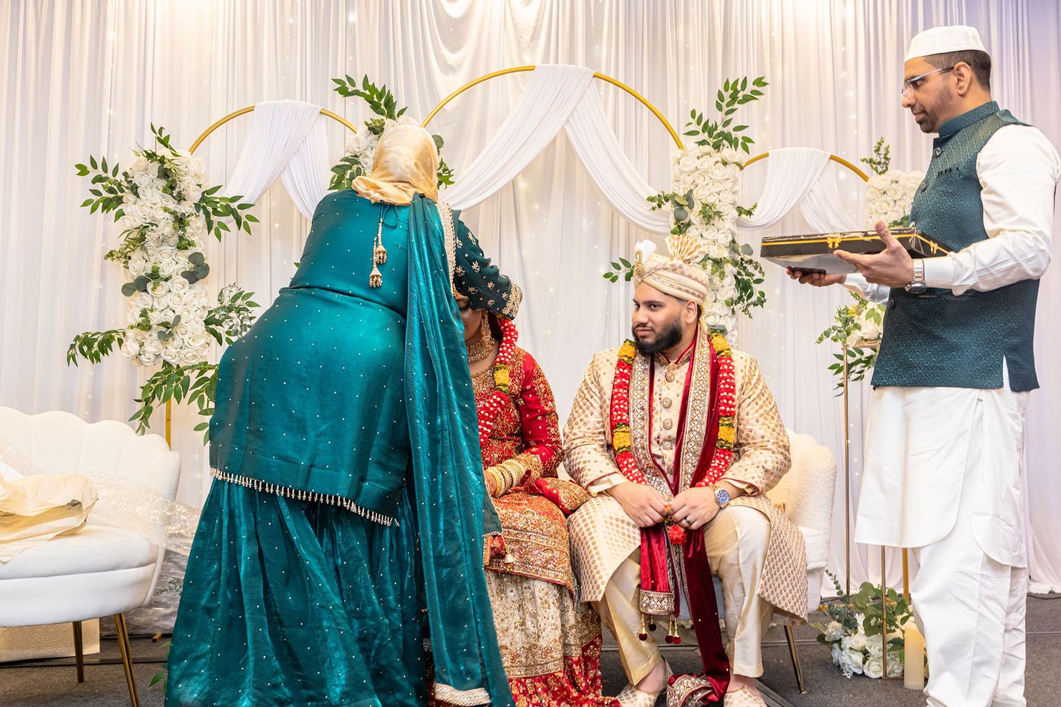 Groom in sherwani sits during traditional South Asian Muslim wedding ceremony with guests.
