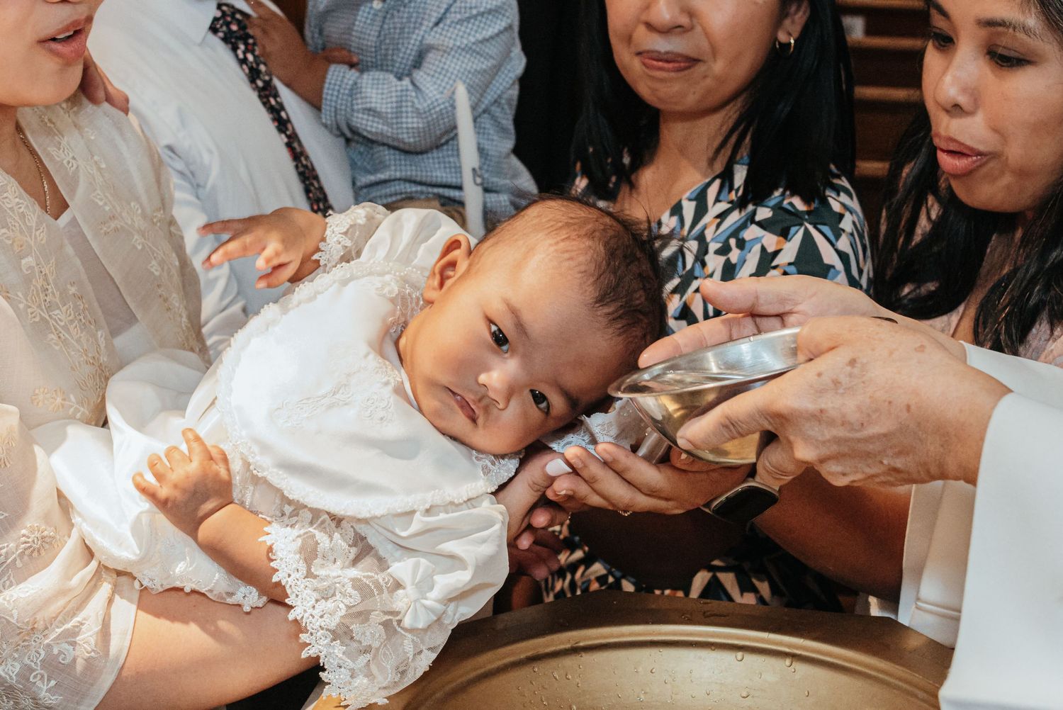 A baby in a white christening gown is baptized with holy water poured over their head.