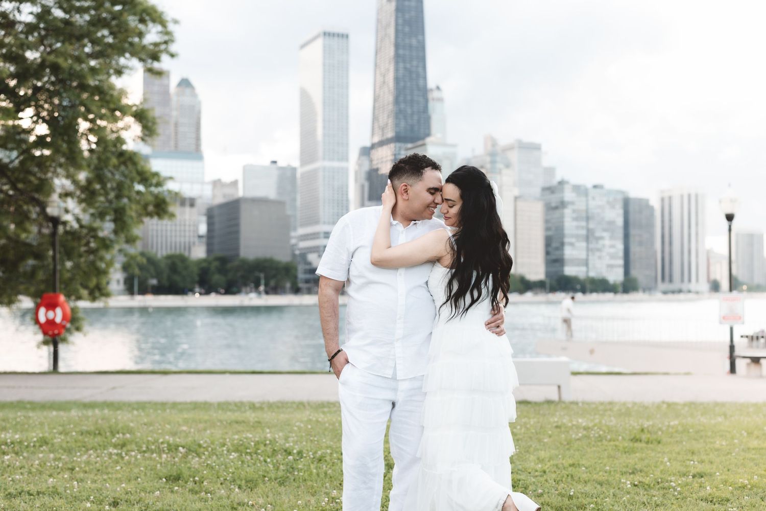 Romantic couple kissing in white attire with Chicago city skyline and waterfront behind them.