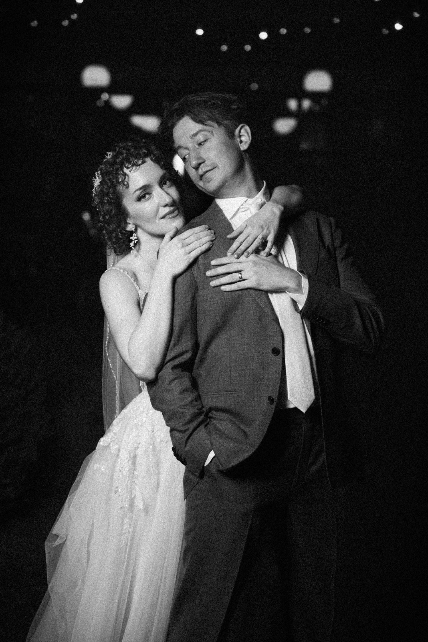 Black and white photo of bride and groom embracing tenderly at night during wedding celebration.