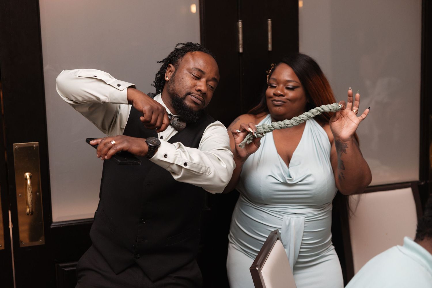 Two wedding guests laugh and dance playfully at lively indoor wedding reception celebration.