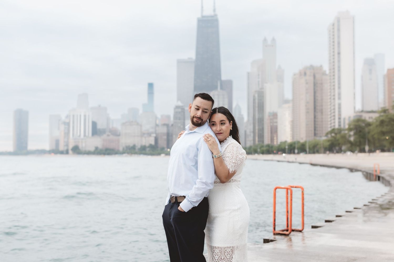 Couple posing romantically by Lake Michigan with Chicago skyline and John Hancock Tower in background.