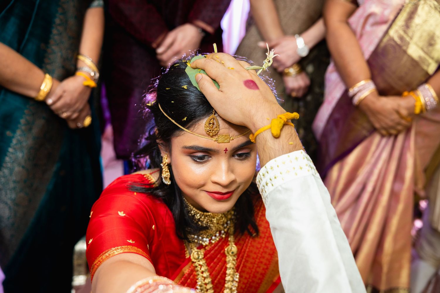 Indian bride in red saree receiving sindoor during traditional Hindu wedding ceremony with gold jewelry.