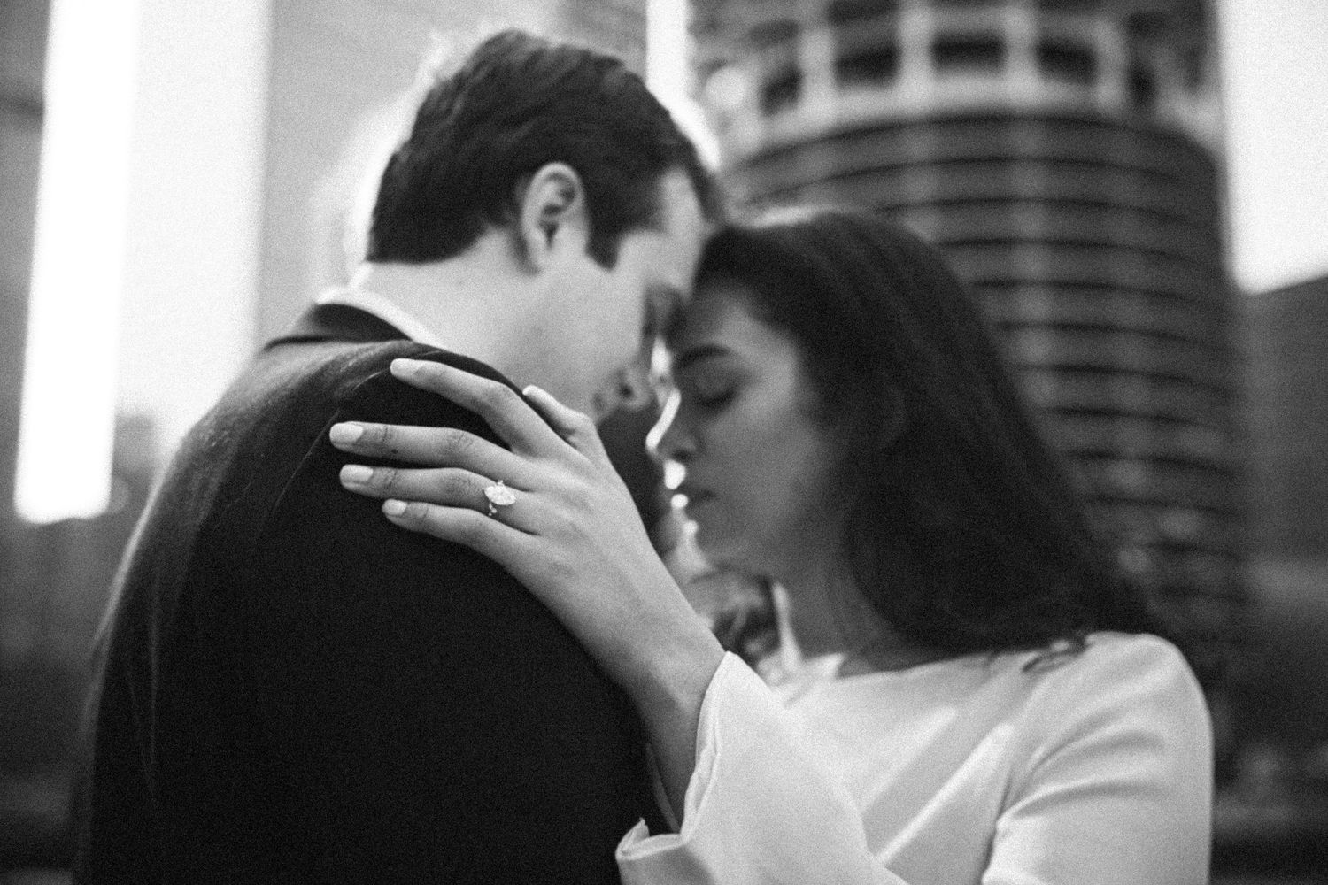 Couple almost kissing with city skyline in background, black and white engagement photo.