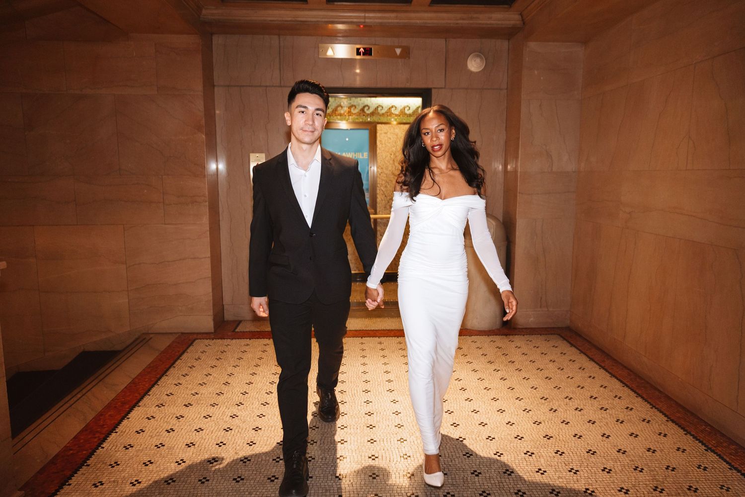 Couple in formal wedding attire holding hands walking through elegant marble hallway together.Chicago Wedding Photographer