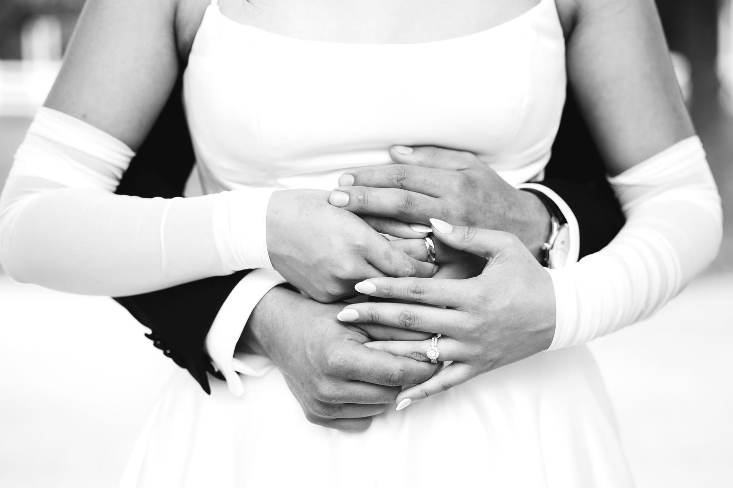 Black and white close-up of bride and groom's hands with wedding rings embracing.