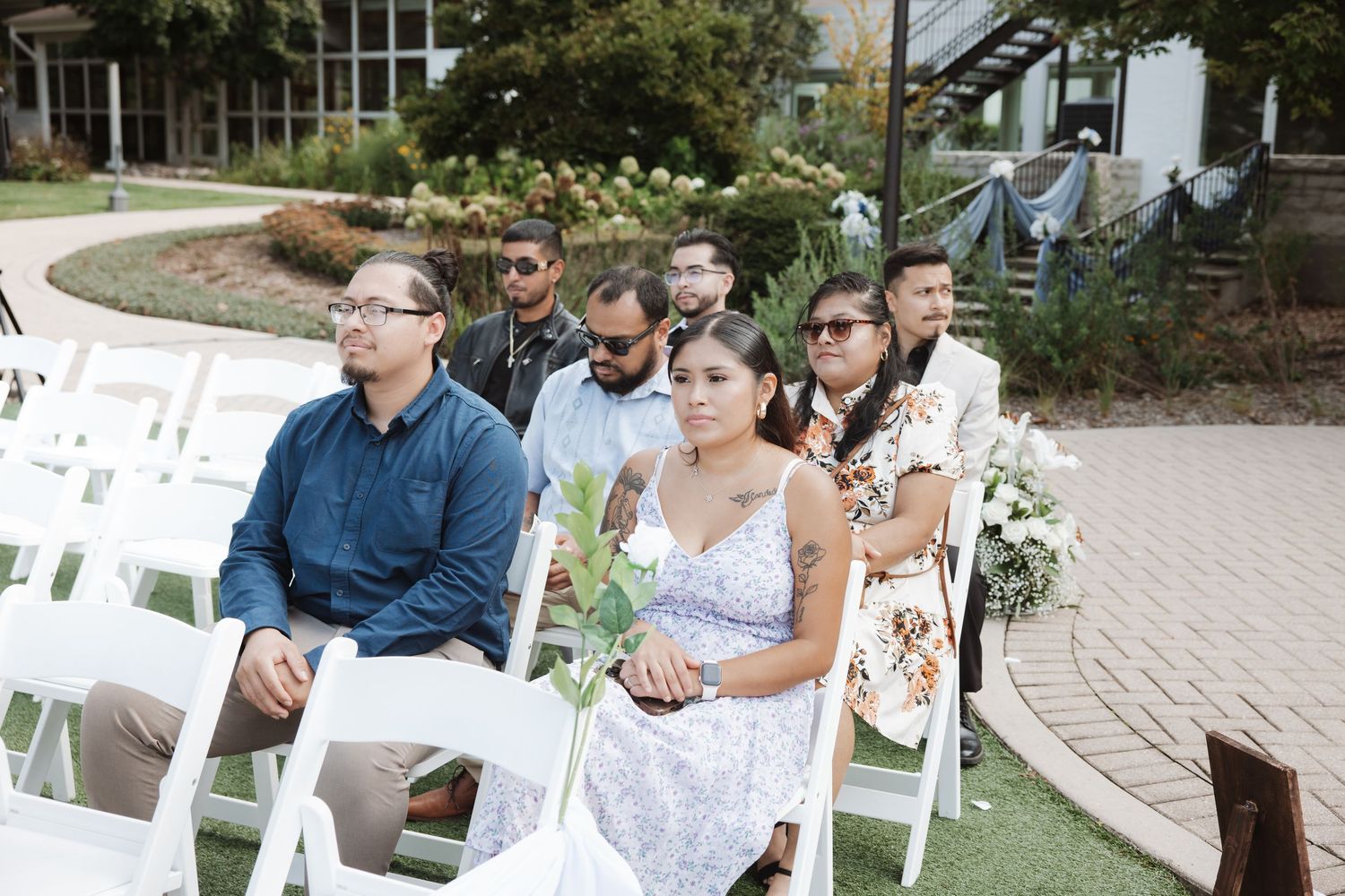 Wedding guests seated in white chairs at an outdoor ceremony, attentively watching the proceedings.