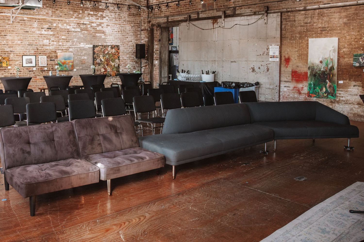 Industrial loft event space with exposed brick walls, modern sofas, and rows of black chairs set up for a presentation.
