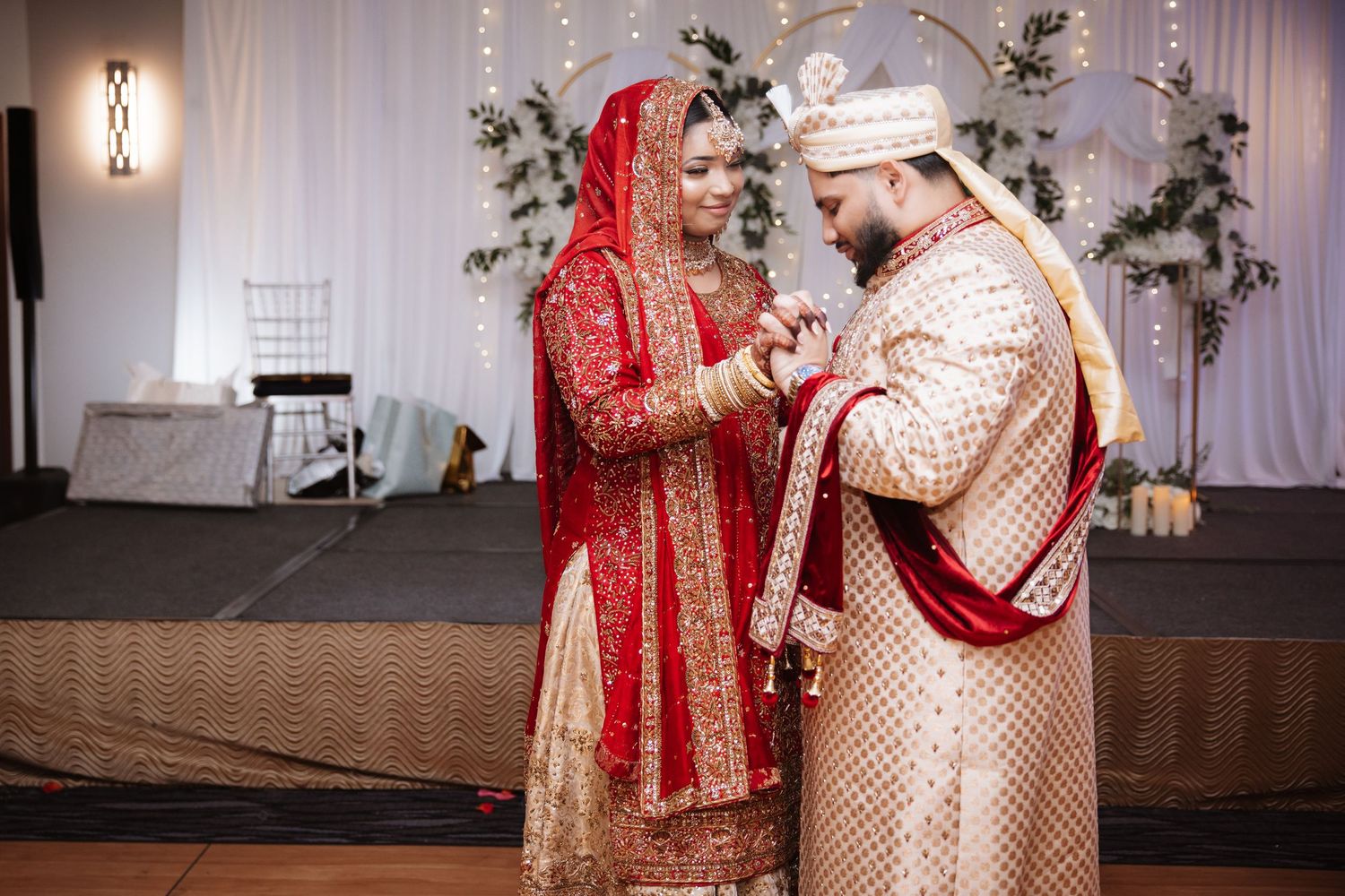 South Asian groom in gold sherwani places ring on brides hand during traditional wedding ceremony.