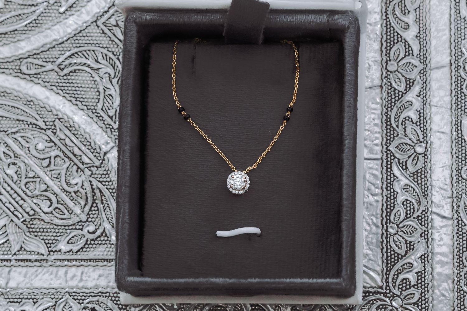 Gold mangalsutra necklace with diamond pendant displayed in dark jewelry box for Indian wedding ceremony.