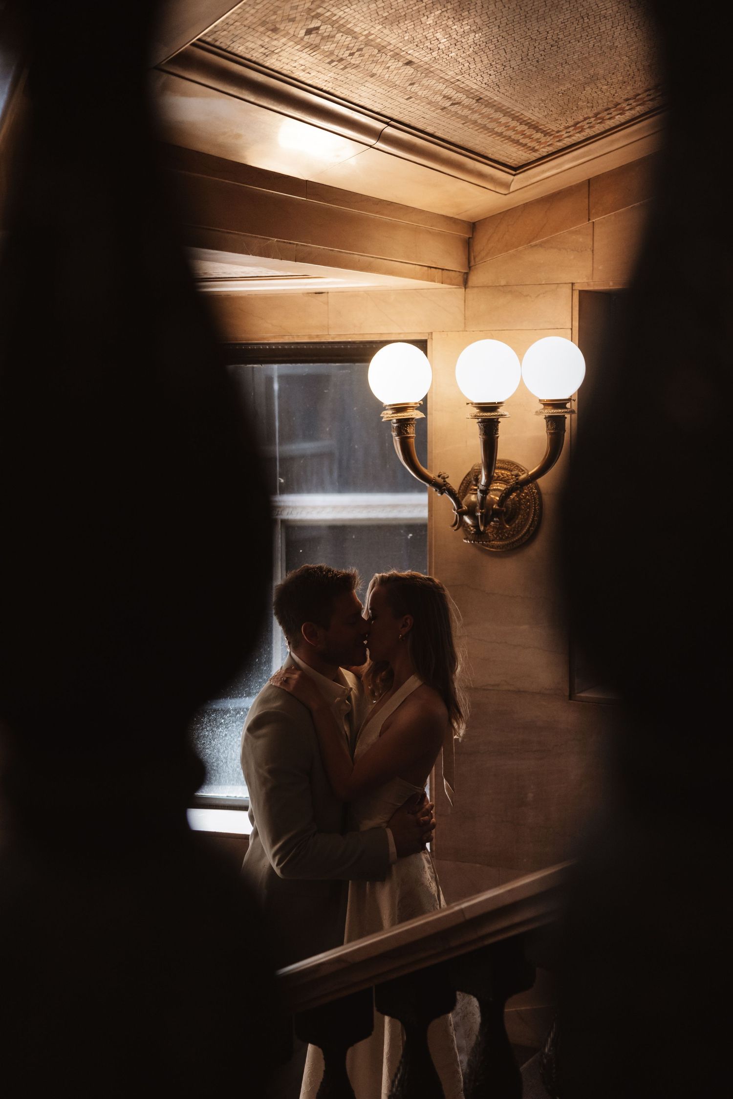Couple shares a kiss framed by warm wall sconces in a dimly lit wedding venue.