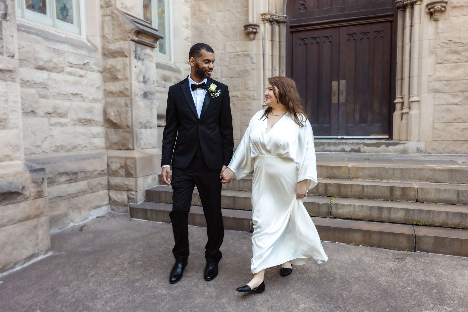 Newlywed couple walking together outside a historic stone church after ceremony.