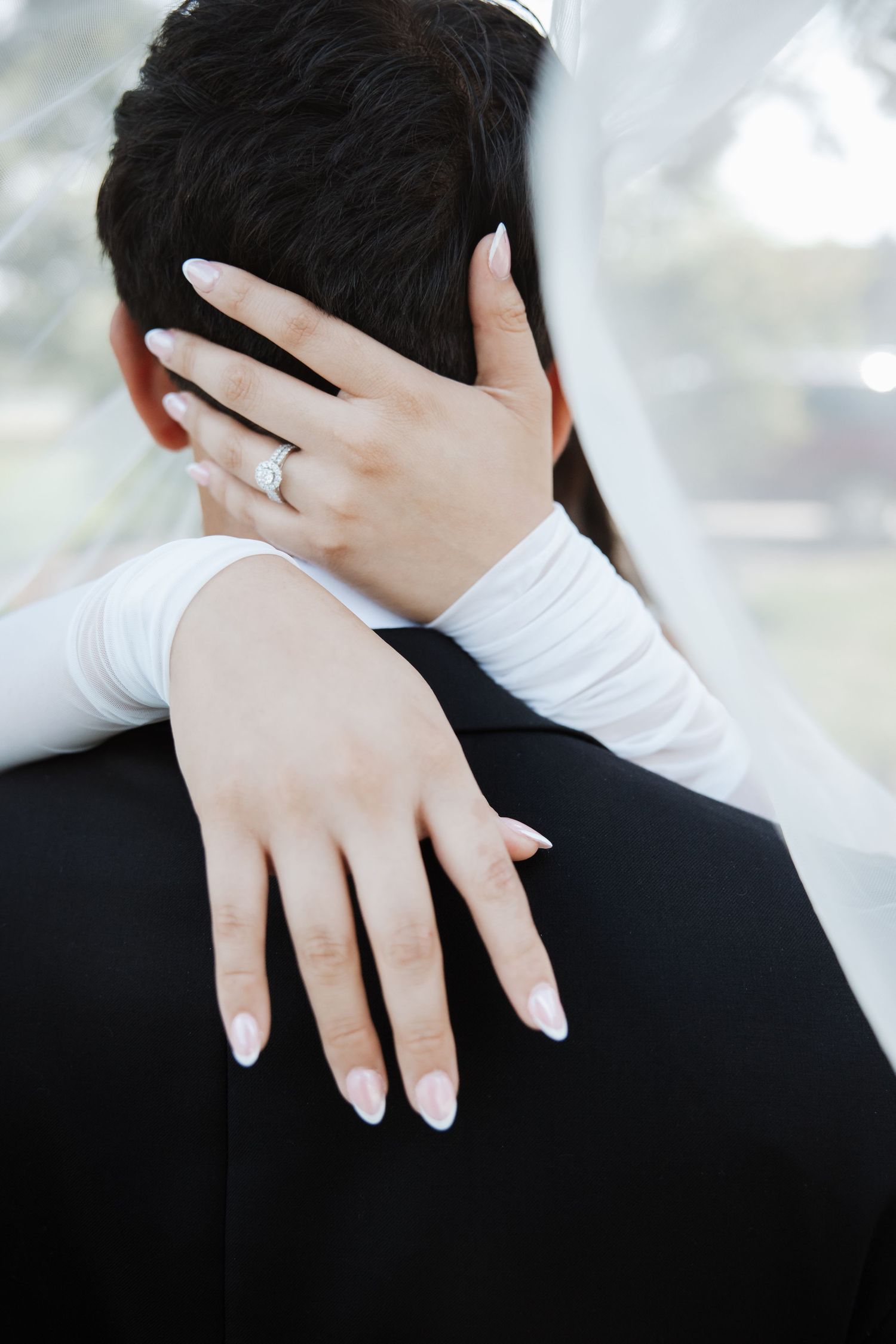 Close-up of bride's diamond ring on hand wrapped around groom's neck at wedding.