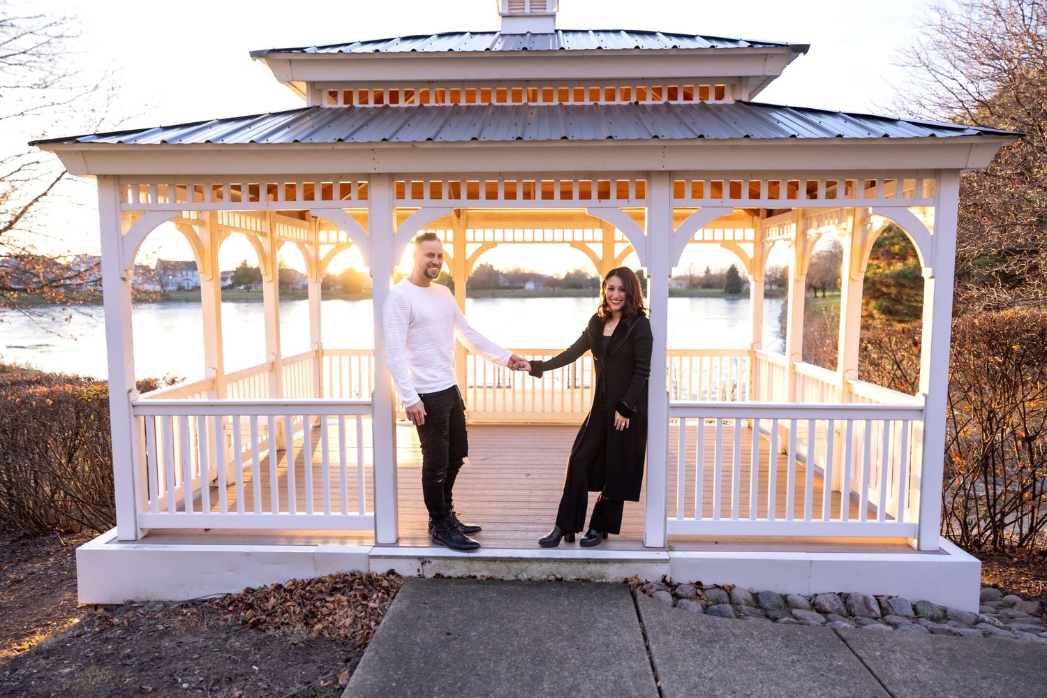 Couple holding hands and posing at a classic white gazebo during a romantic outdoor engagement photo session.