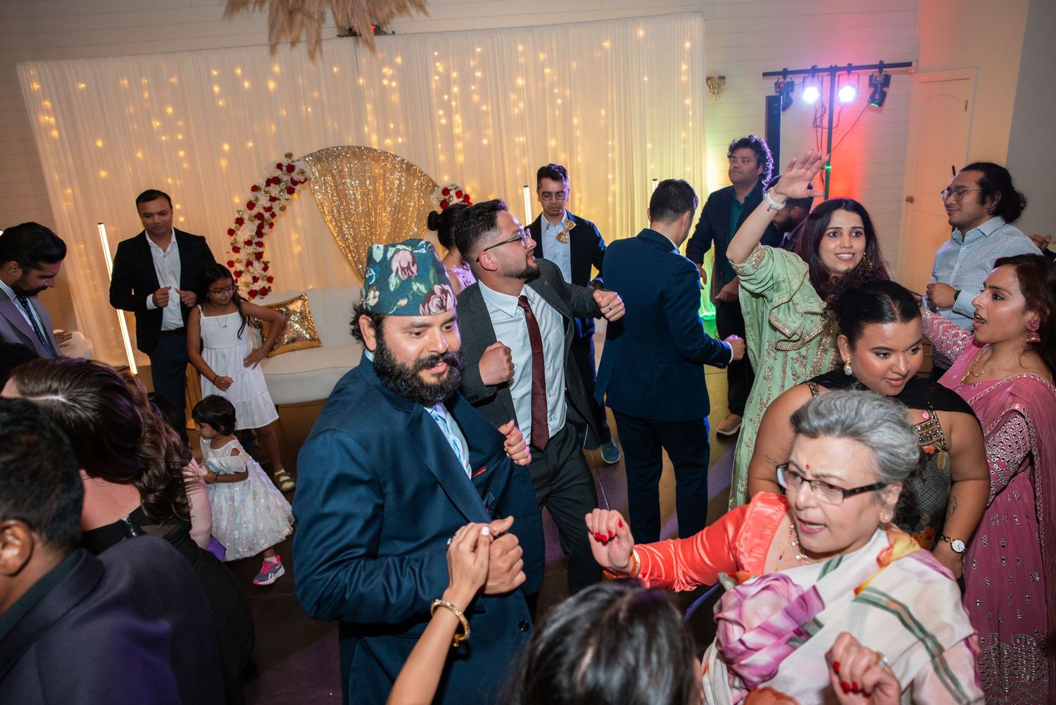 Wedding guests dancing energetically at a festive reception with decorative lighting.