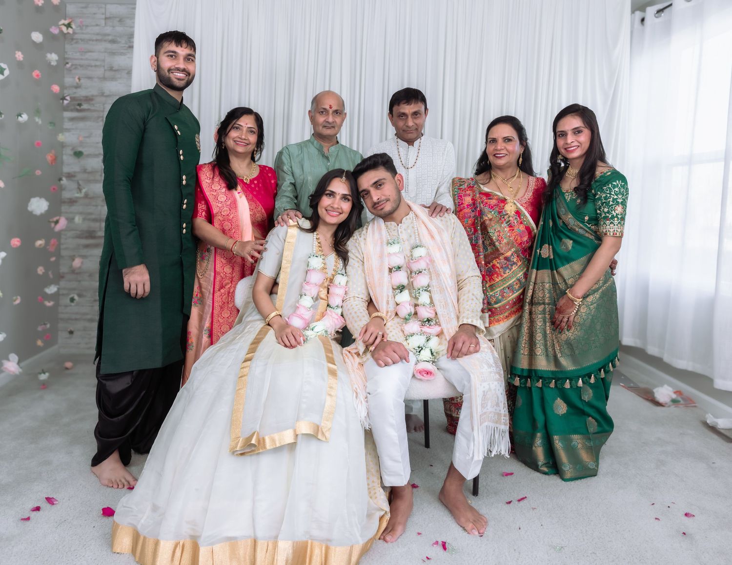 Wedding family group photo with bride and groom seated as confetti falls in a bright white venue.