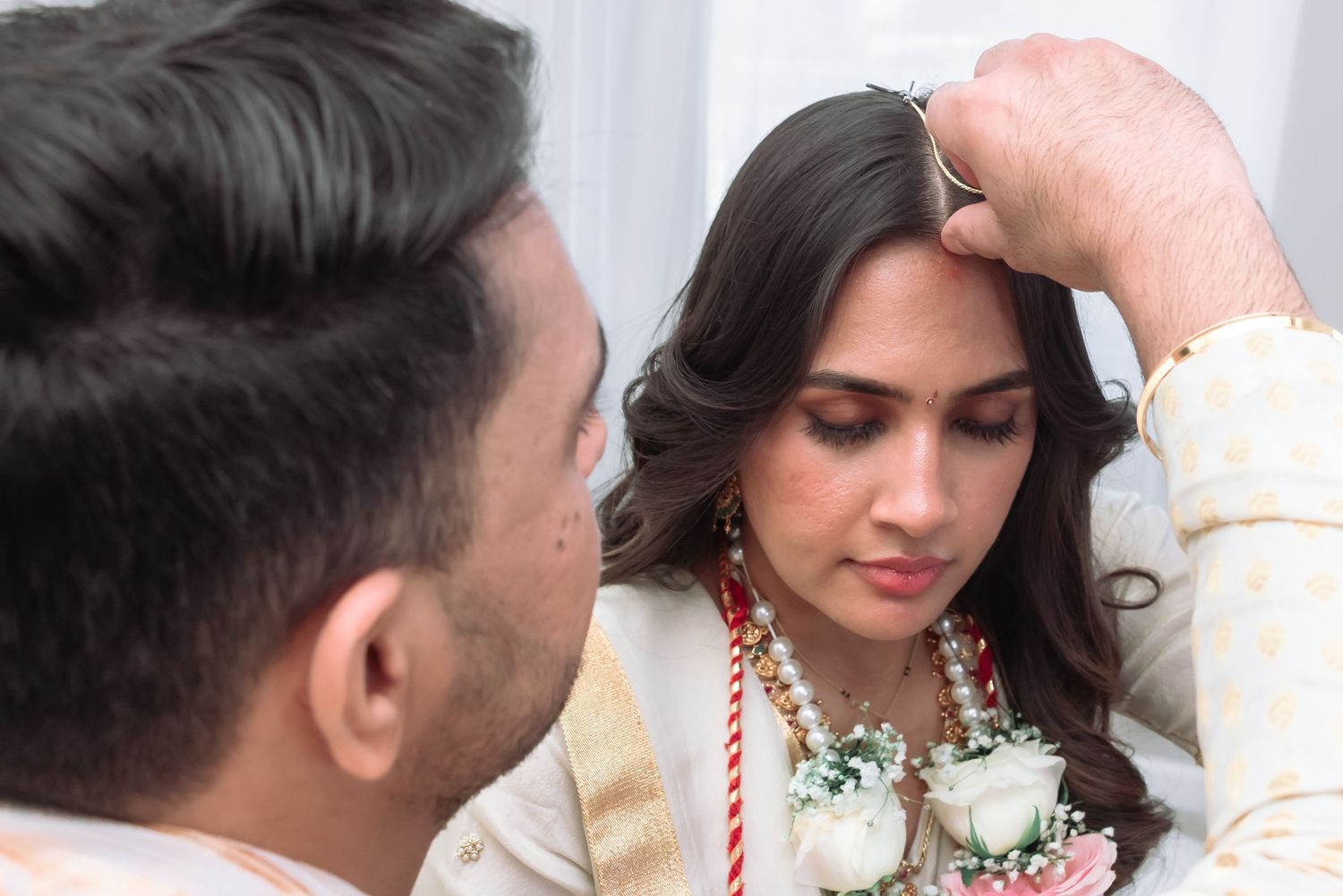 Close-up of groom applying sindoor to bride during traditional Indian Hindu wedding ceremony.