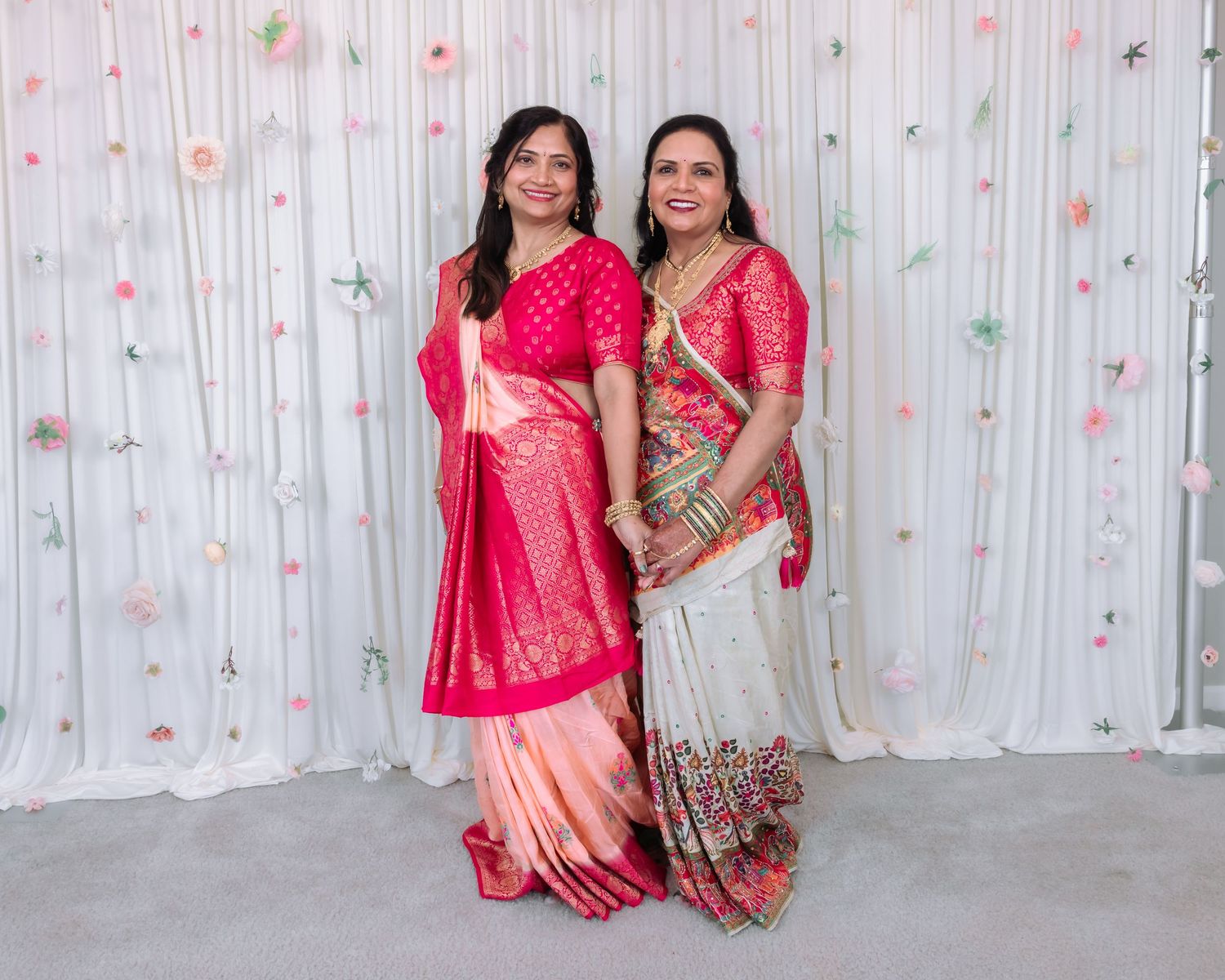Two Indian women posing together in pink sarees at a traditional wedding event.