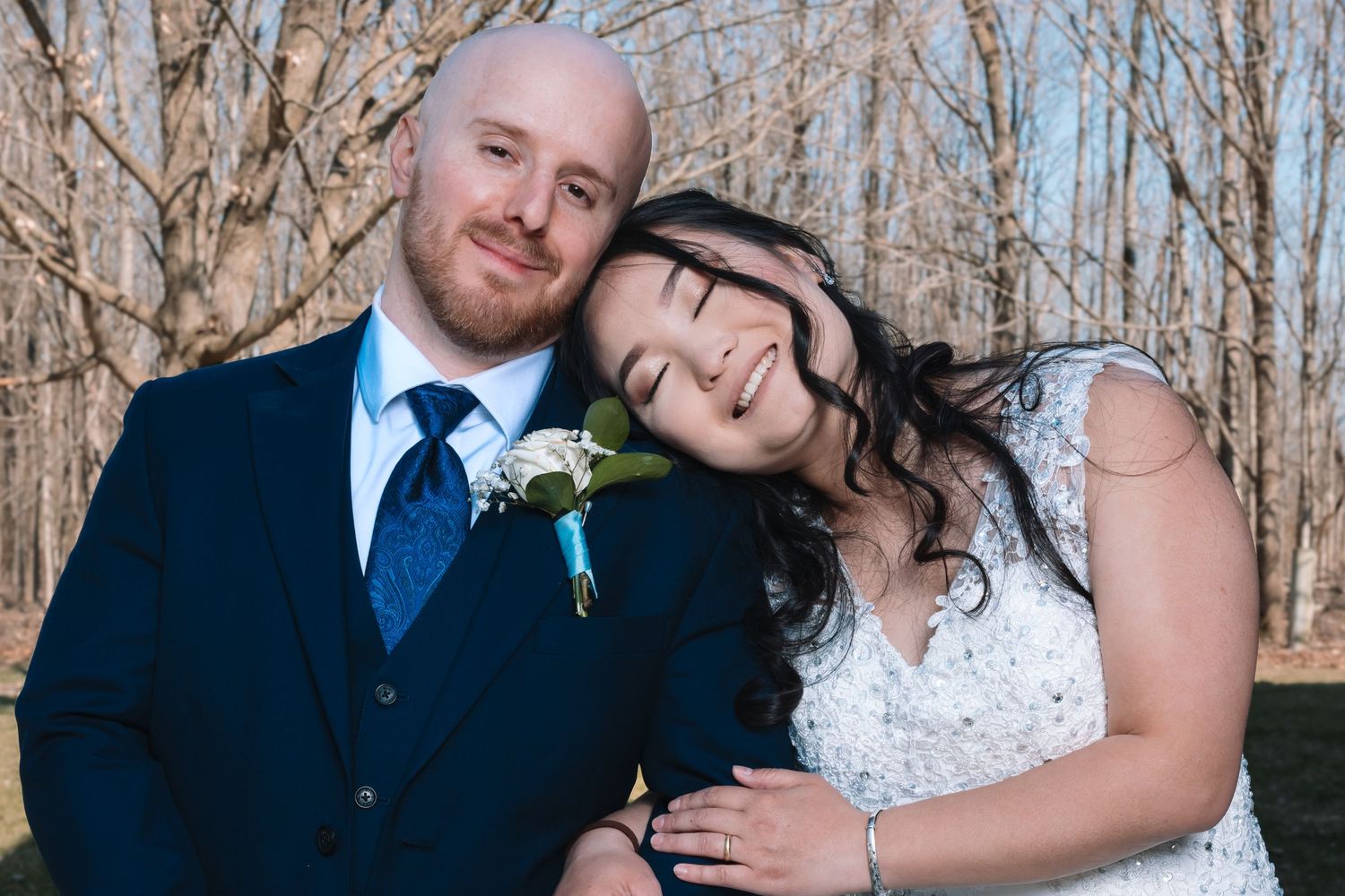 Bride resting head on groom's shoulder in a tender wedding portrait outdoors.
