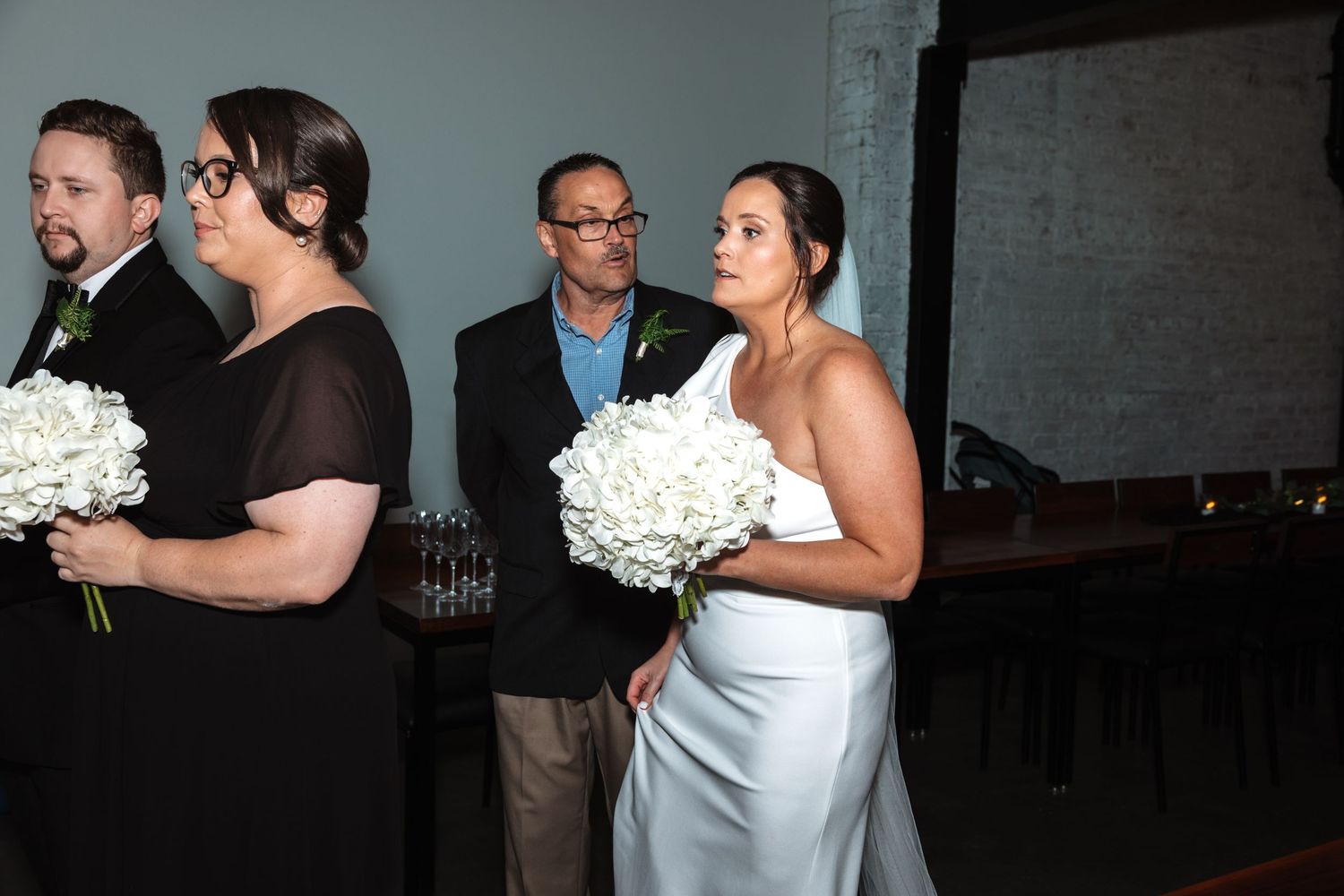 Bridesmaid in black dress holding white hydrangea bouquet standing beside bride in white gown.
