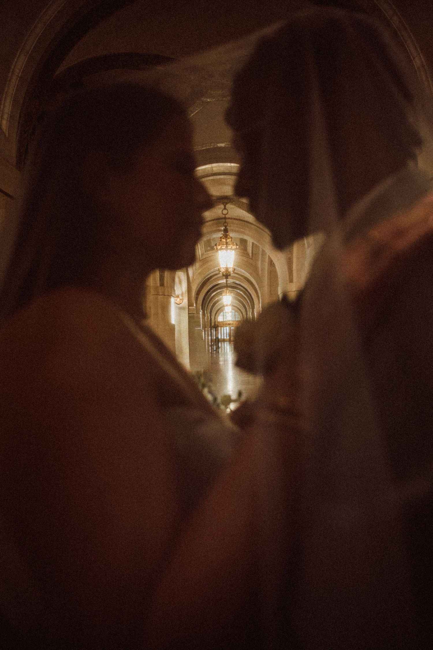 Silhouetted couple sharing an intimate moment in an elegant warmly lit hallway with arched ceilings and chandelier.