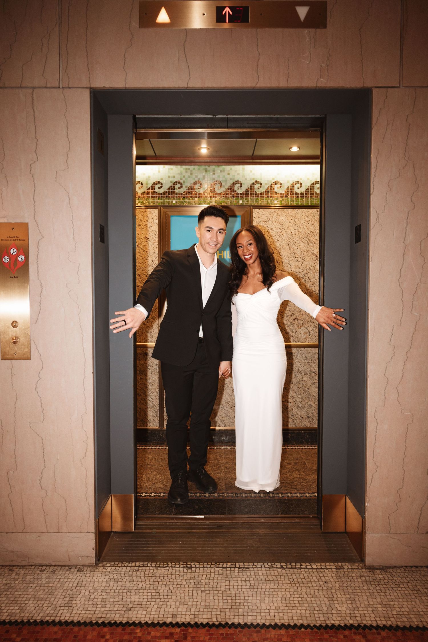 Celebrating couple with open arms smiling in elevator doorway wearing black suit and white bridal gown.Chicago Wedding Photographer