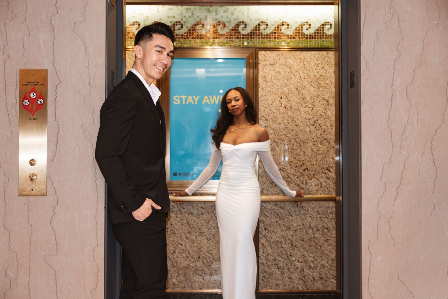 Elegant couple posing in an ornate elevator, man in black suit and woman in white off-shoulder gown.Chicago Wedding Photographer