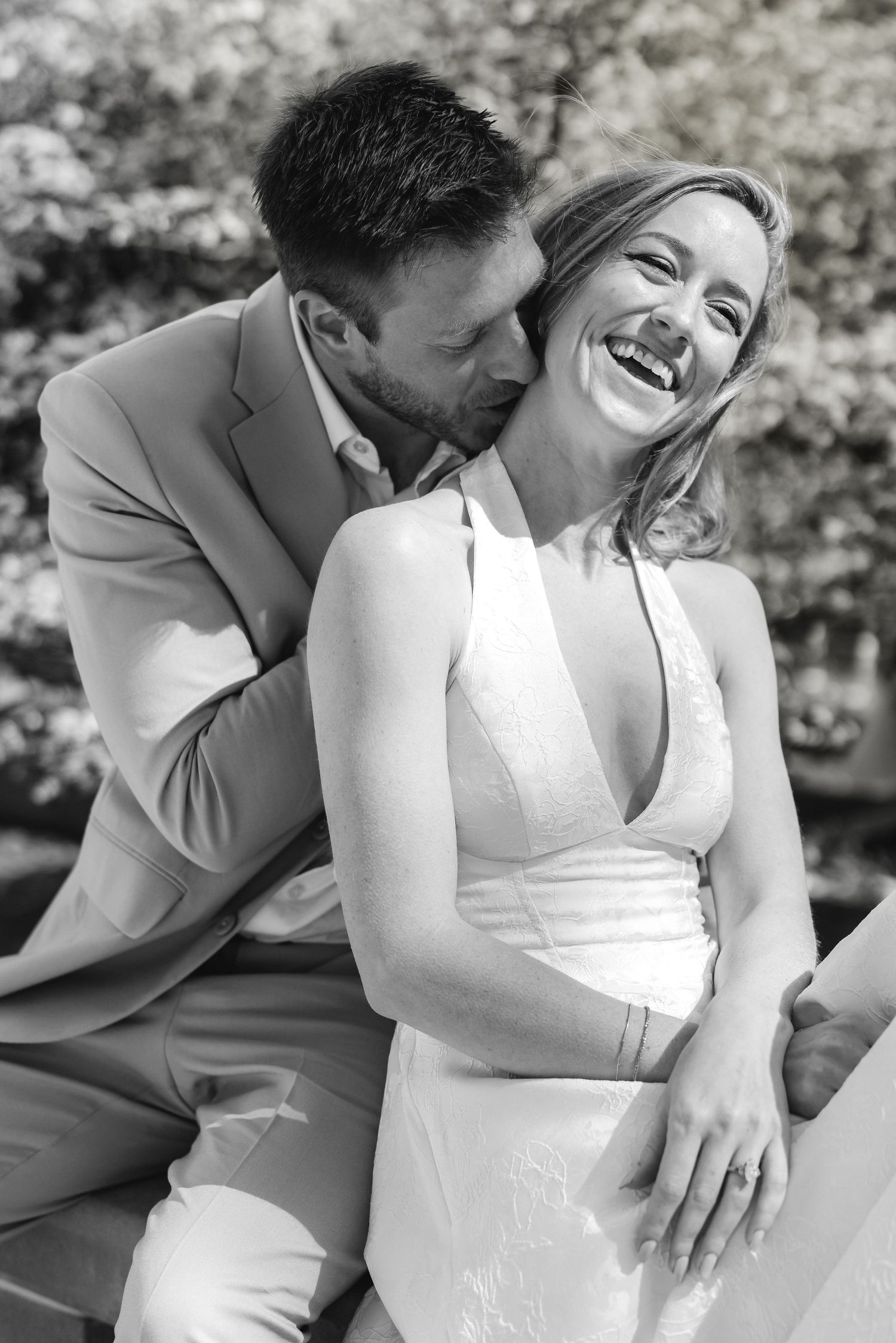 Black and white photo of laughing bride and groom sharing a joyful moment outdoors.