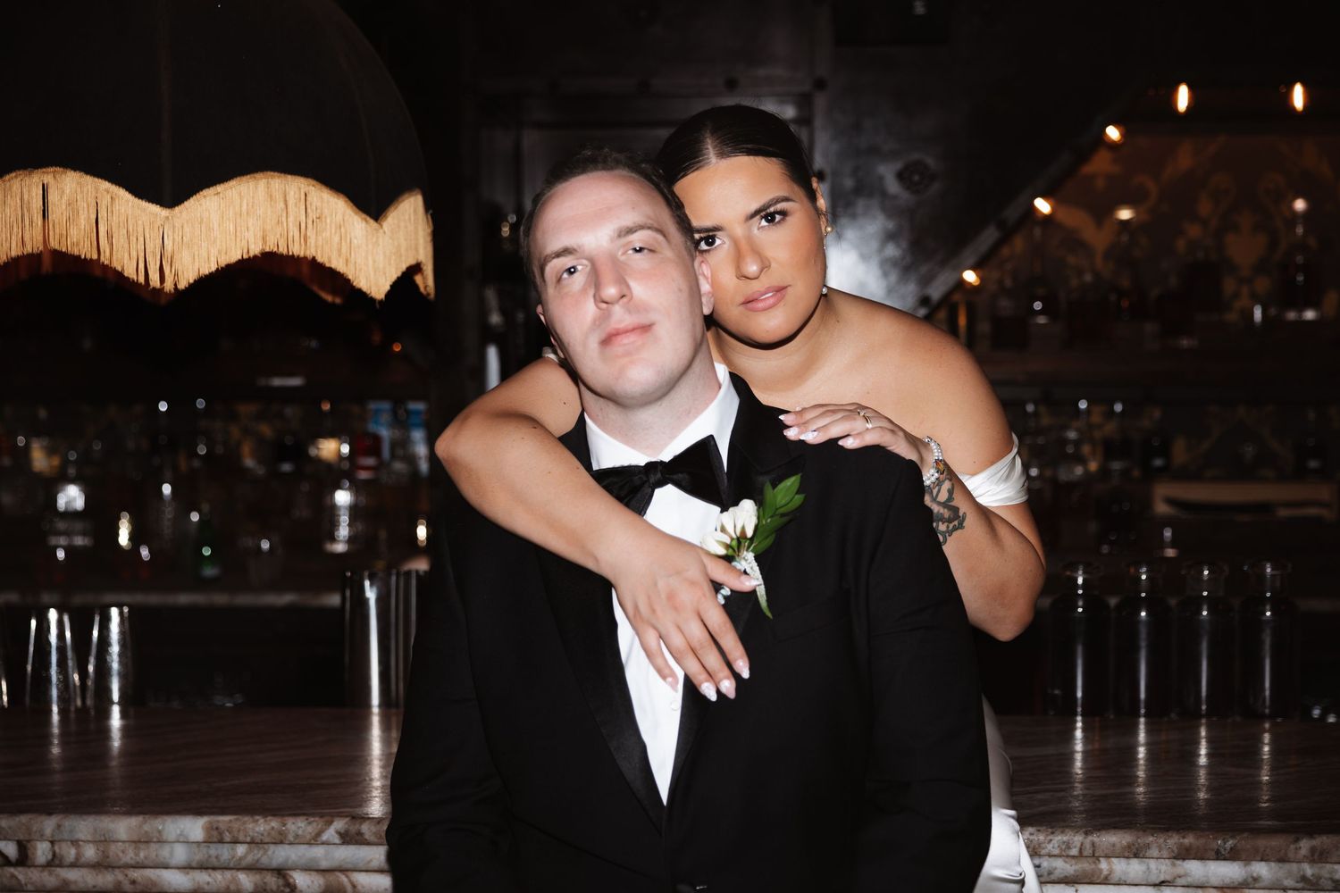A couple in formal wedding attire pose together with the groom wearing a white boutonniere corsage.