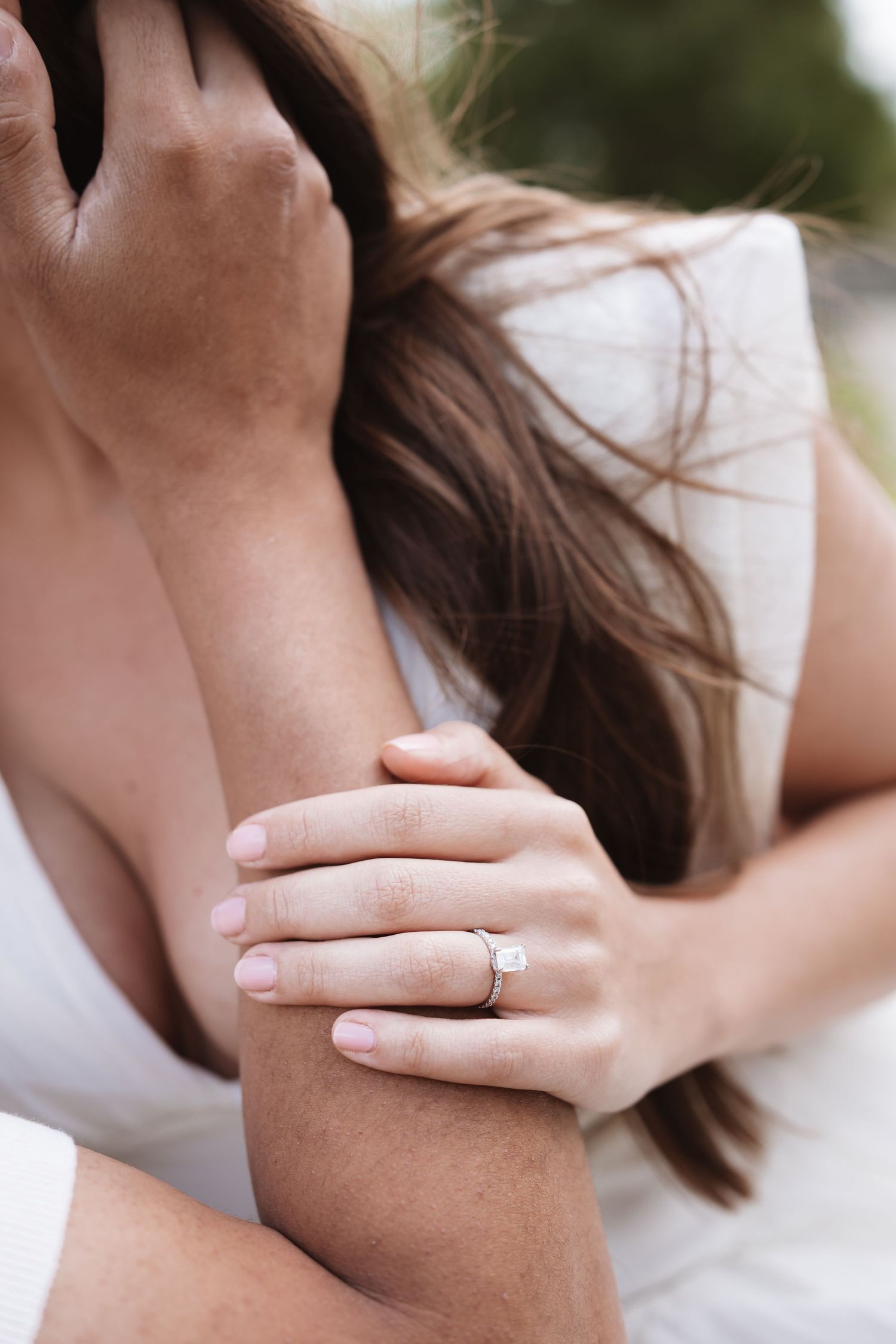Close-up of womans hand with diamond engagement ring while embracing partner outdoors.
