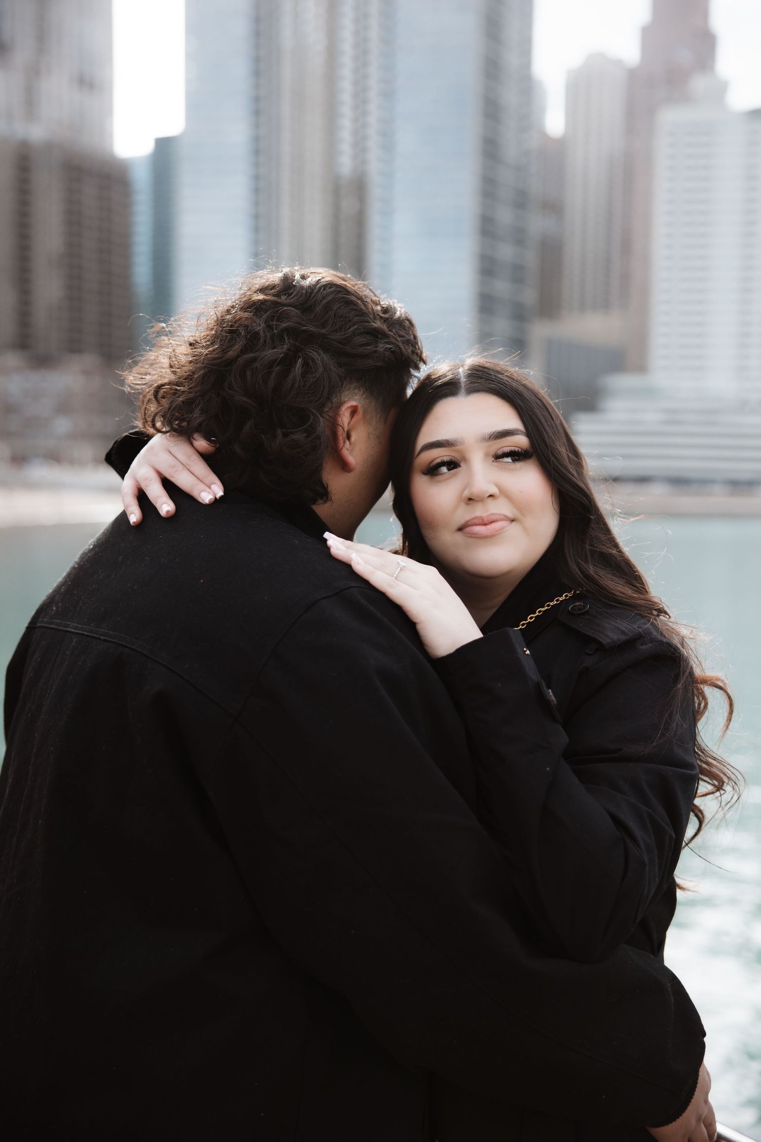 Woman smiles embracing partner near Chicago River with blurred city skyline background.