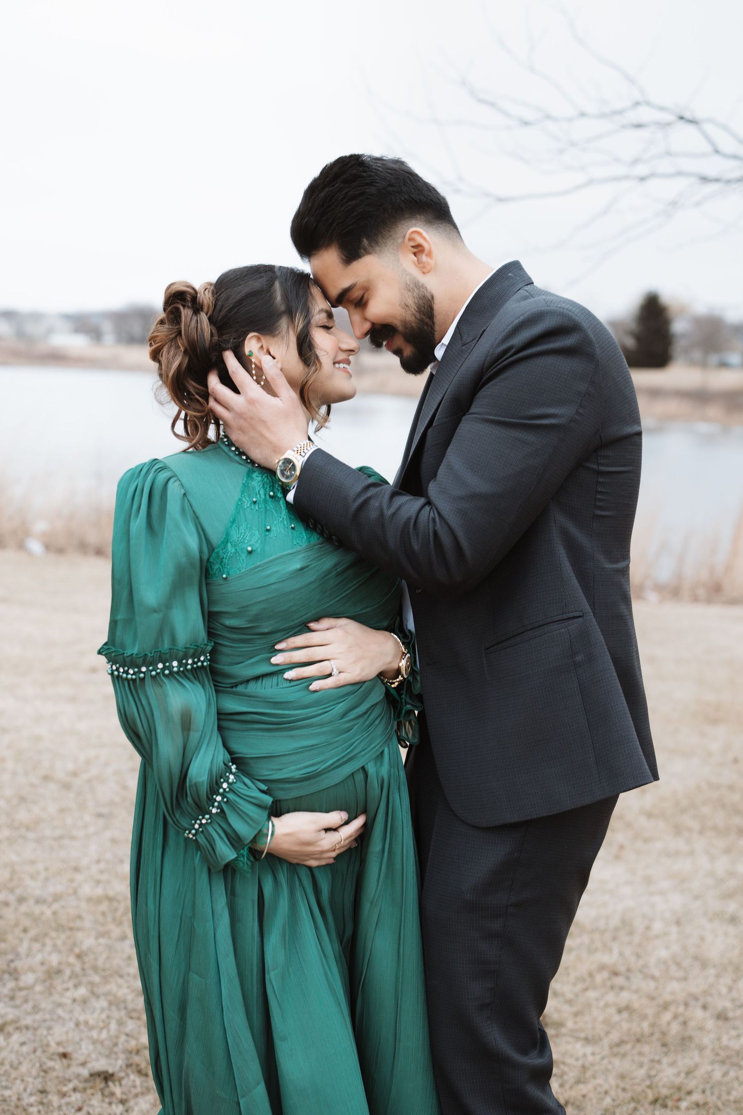 Couple sharing tender forehead touch moment outdoors, man in suit embracing pregnant partner.