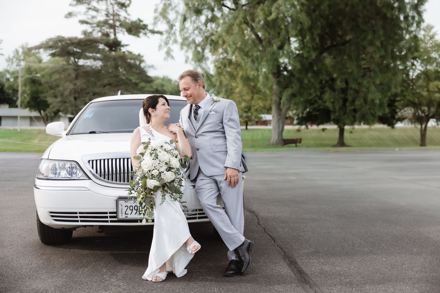 Bride and groom posing together in front of a white Lincoln stretch limousine on their wedding day.