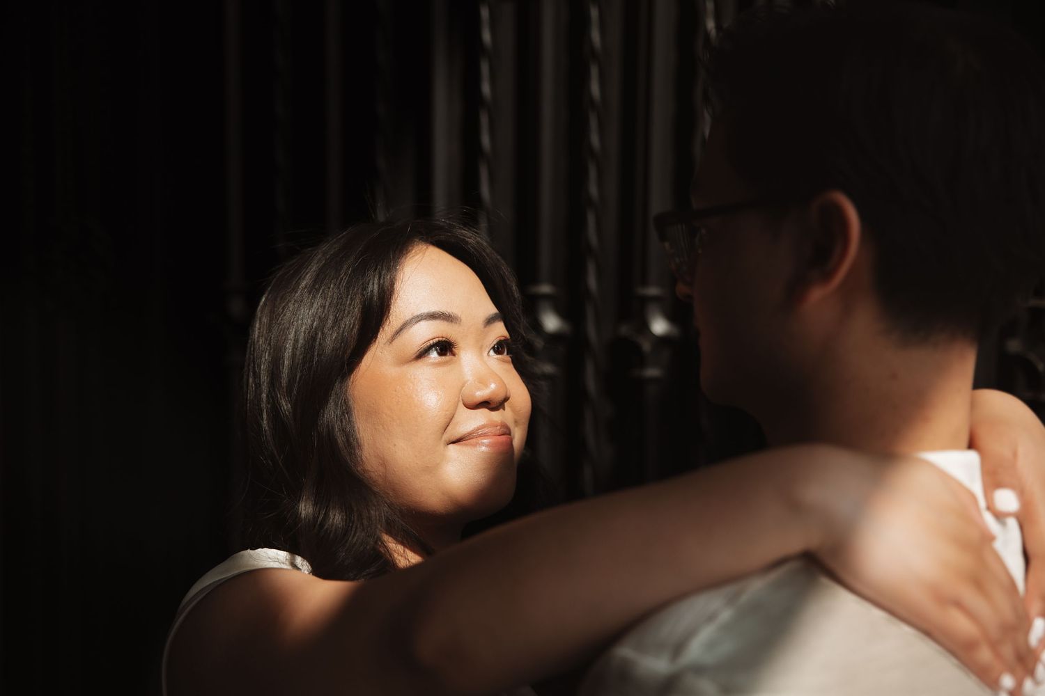 Woman gazes lovingly upward while embracing partner in dramatic lighting.