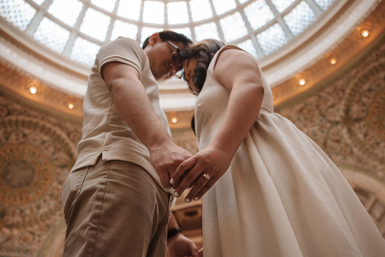 Couple holds hands under ornate domed ceiling during wedding ceremony.