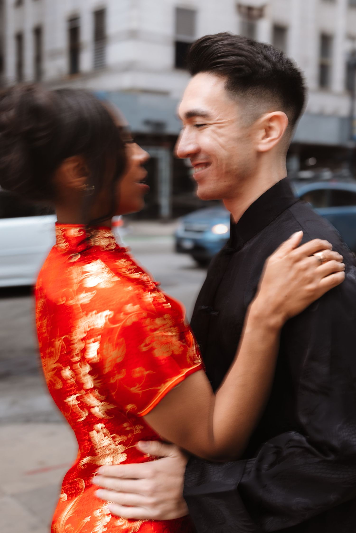 Smiling interracial couple embracing on city street, woman in red cheongsam and man in black tang suit.

Chicago Wedding Photographer