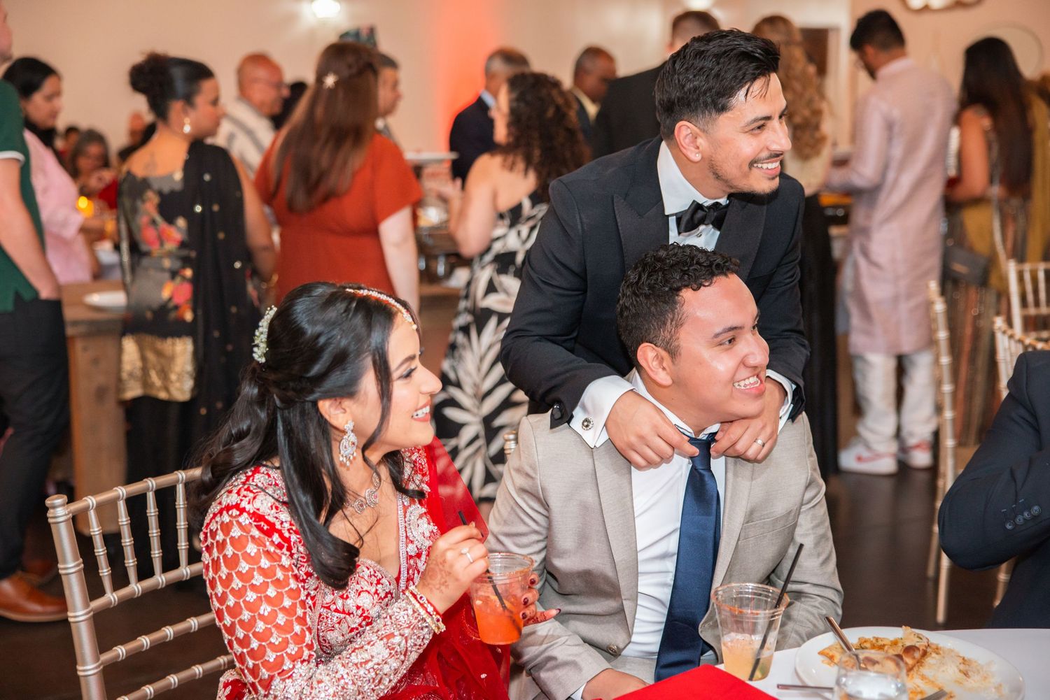 Man in tuxedo posing with seated couple at festive wedding reception.
