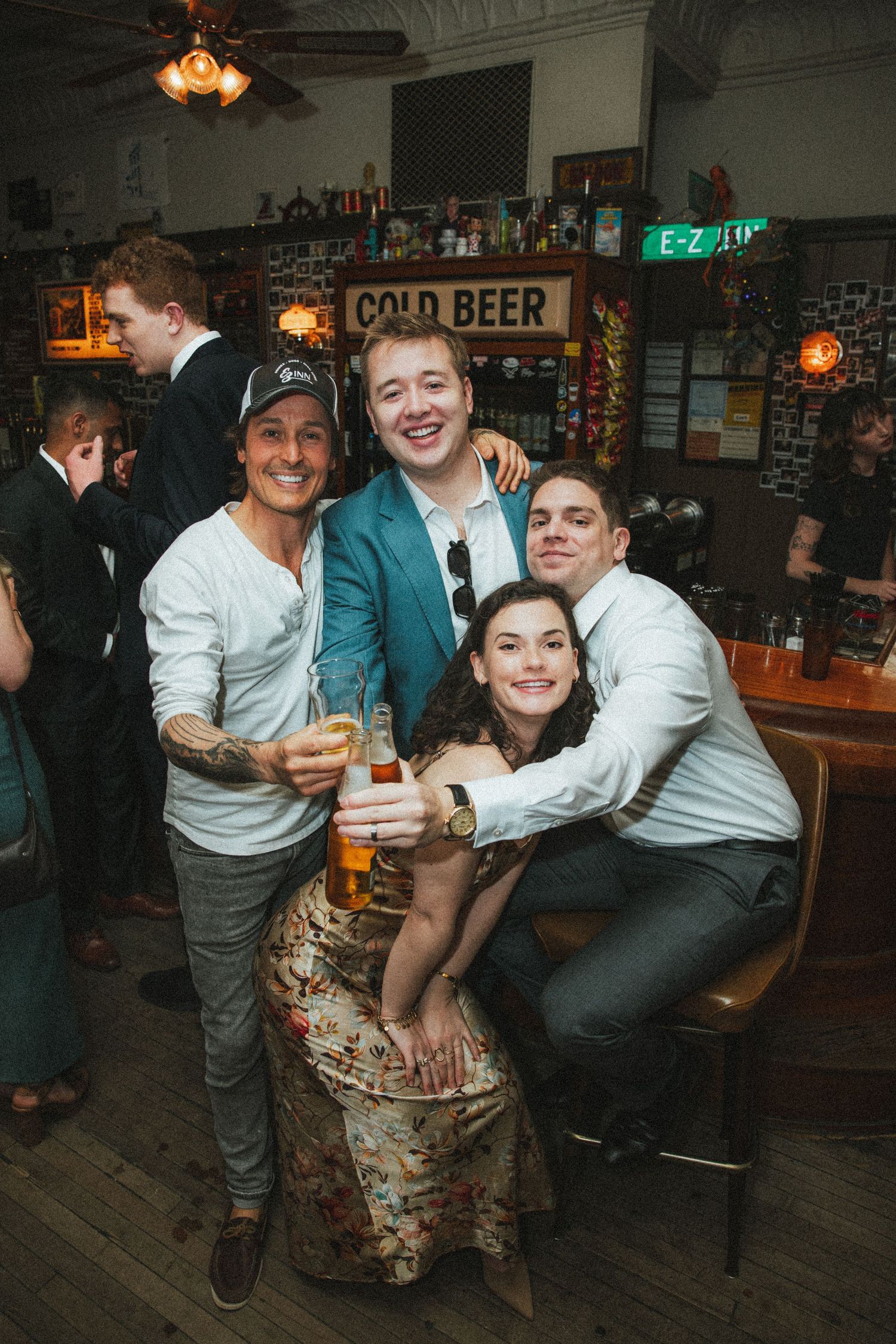 Four friends happily pose together holding drinks at a lively bar celebration event.