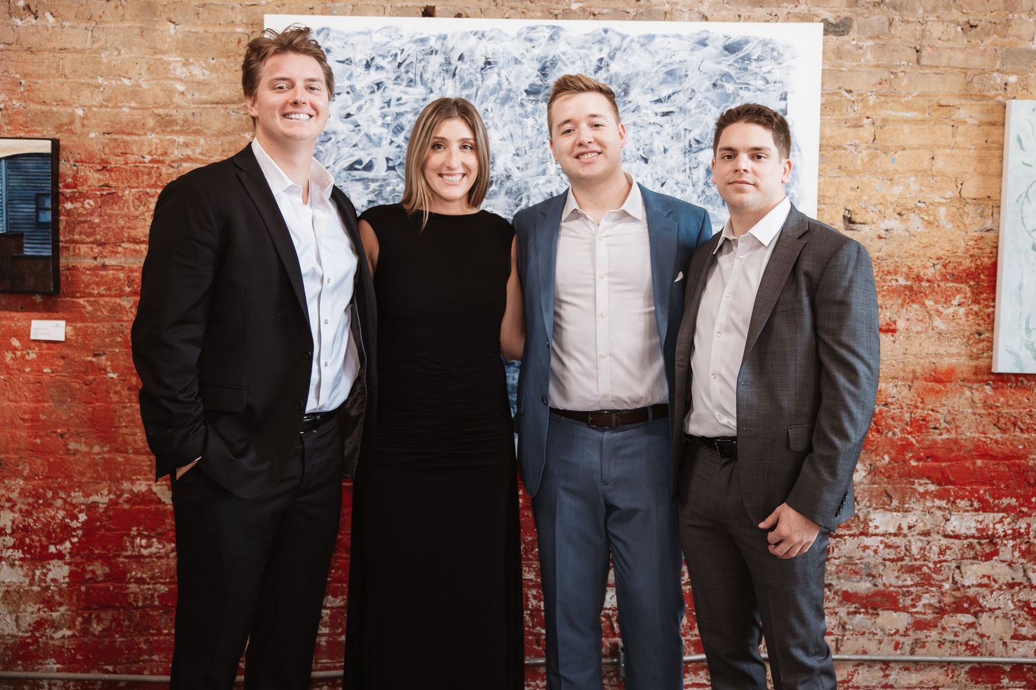 Four professionals smiling together at an art gallery event with blue abstract painting backdrop.