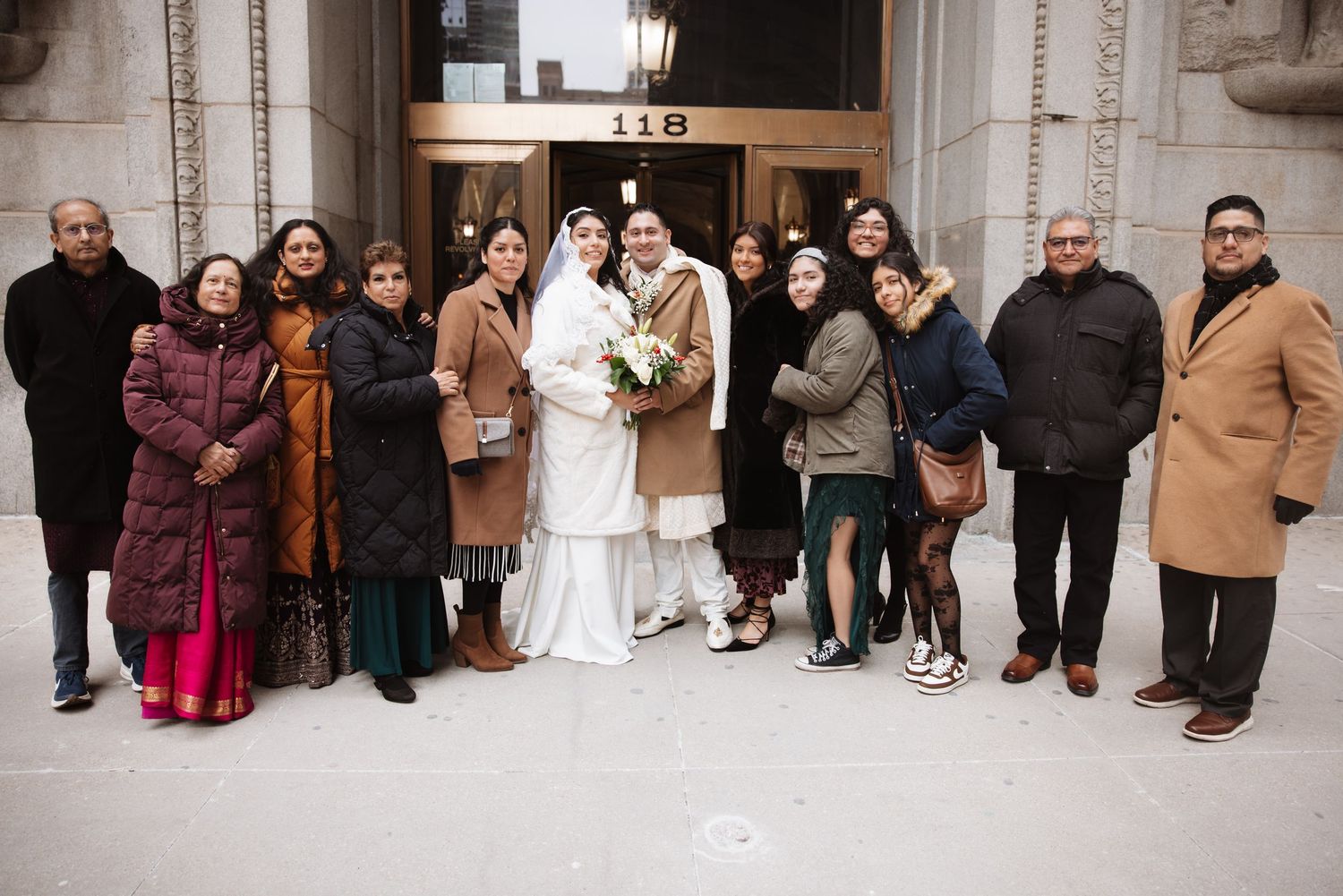 Newlyweds posing with family members outside a Chicago building entrance in winter coats.