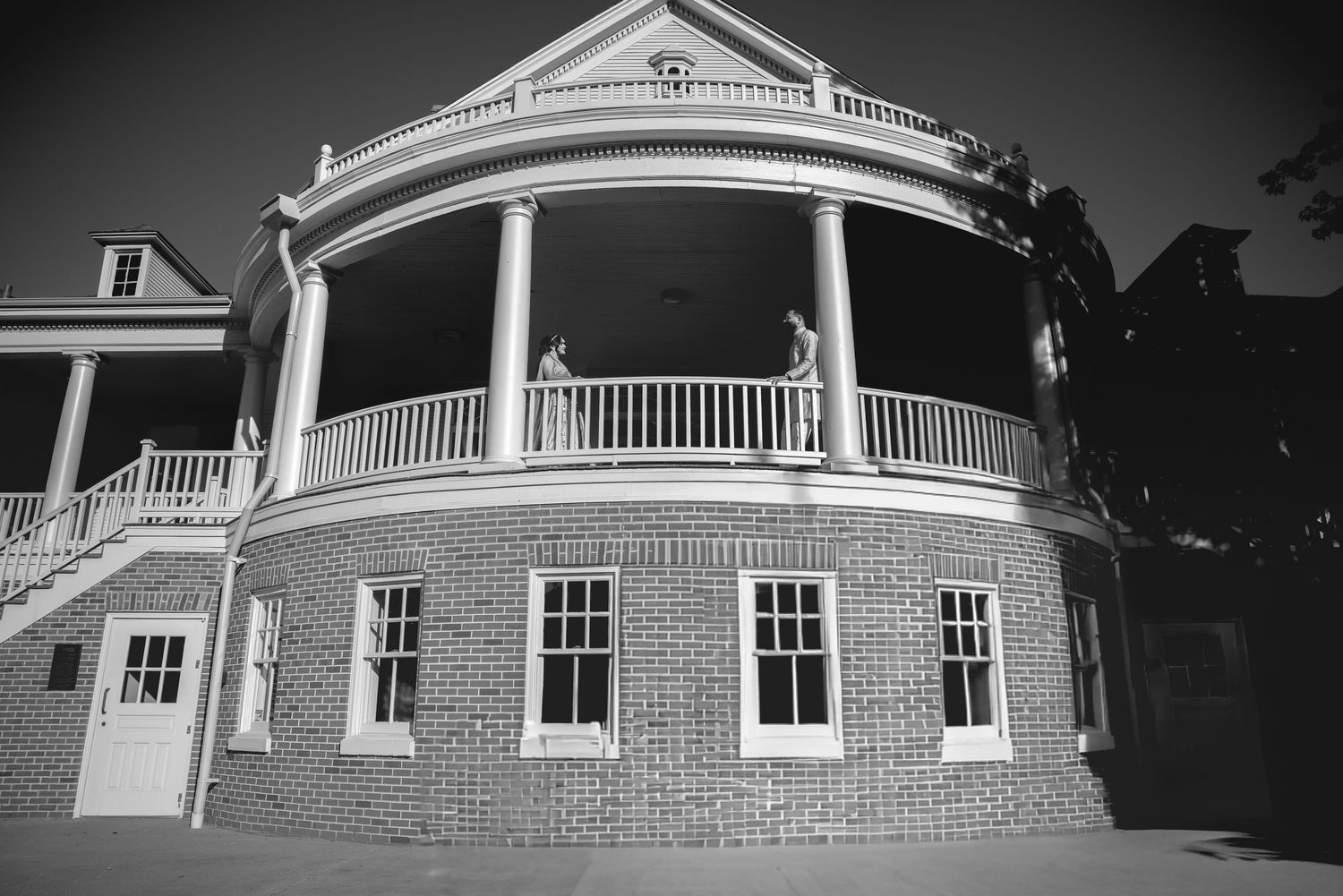 Black and white photo of a grand brick building with curved white balcony and classical architectural details.