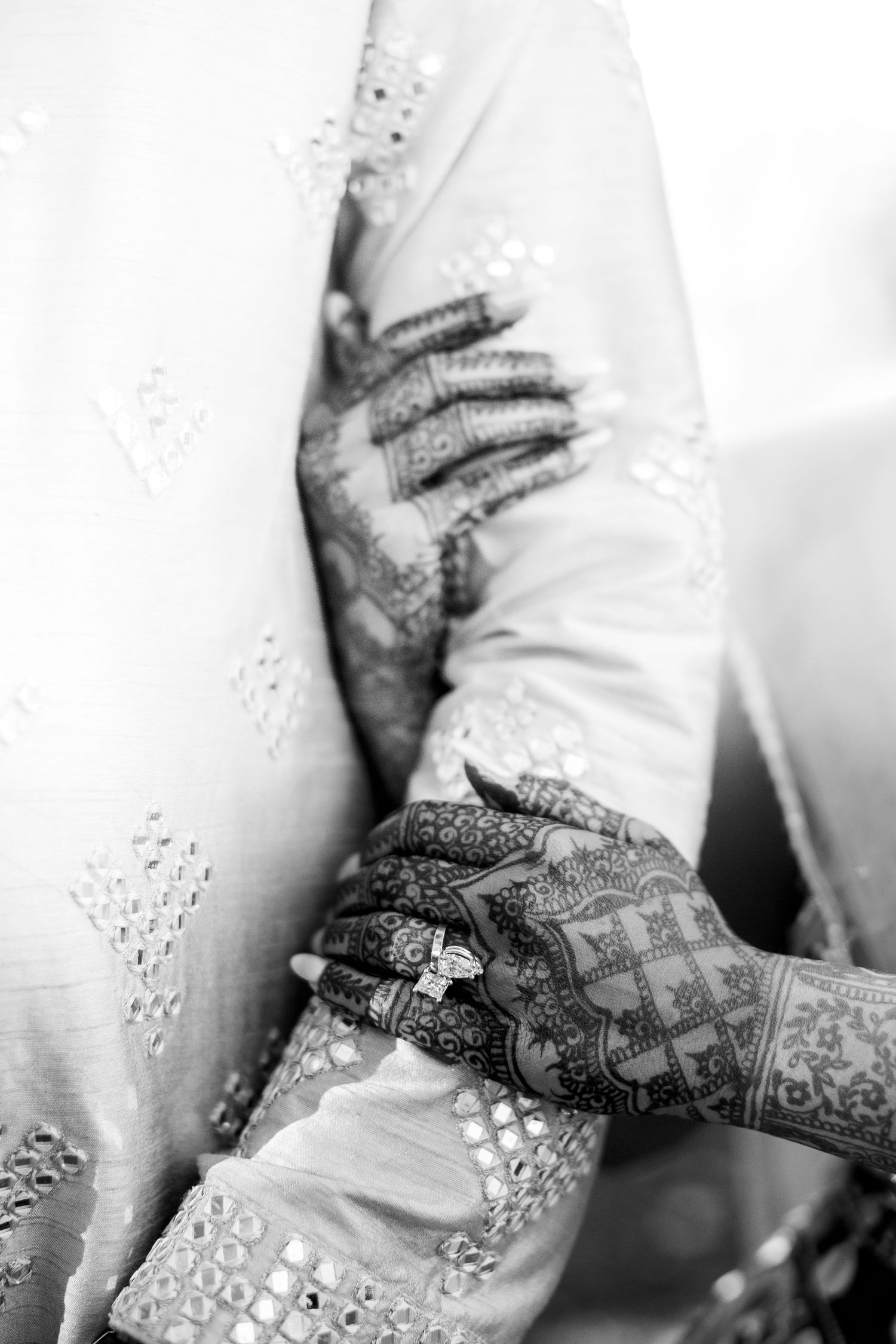 Black and white close-up of brides hands with detailed henna mehndi patterns and sparkling engagement ring.