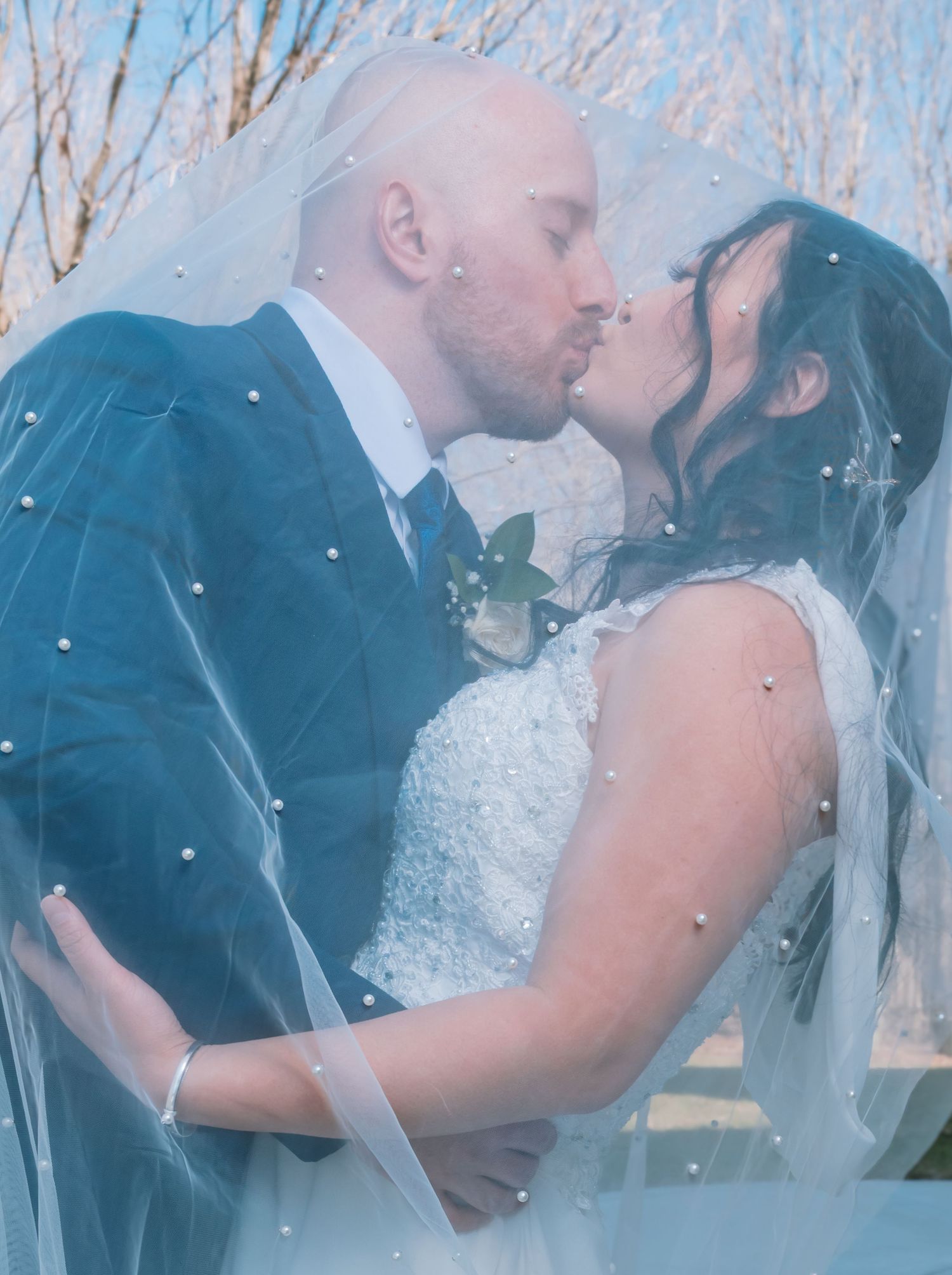 Bride and groom share a passionate kiss under a pearl-dotted wedding veil on their winter wedding day.