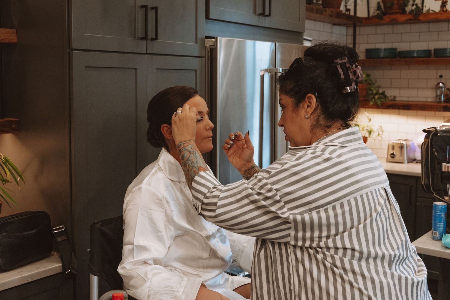 Makeup artist applying foundation to a bride's face in a modern kitchen during wedding preparations.