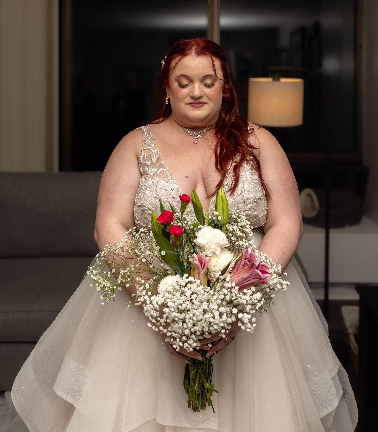 Bride with auburn hair in lace bodice gown holds mixed bouquet of tulips and baby's breath.