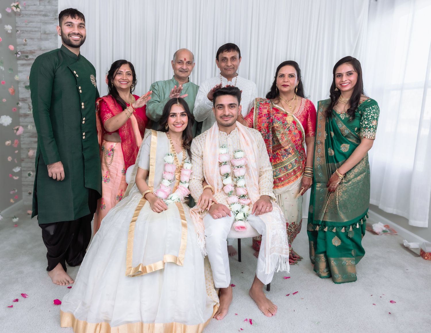 Wedding party group photo at Indian engagement ceremony with seated couple wearing garlands.