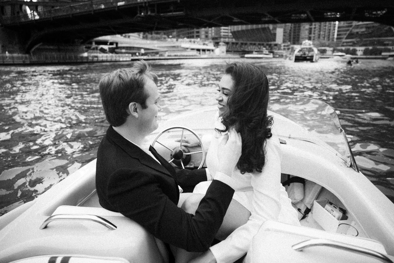 Couple sharing a romantic moment on a speedboat on an urban river in black and white.