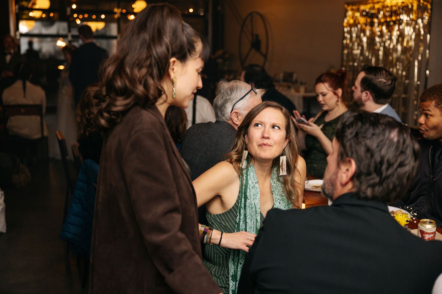 Guests mingling at an elegant indoor wedding reception with warm ambient lighting and chandelier in background.