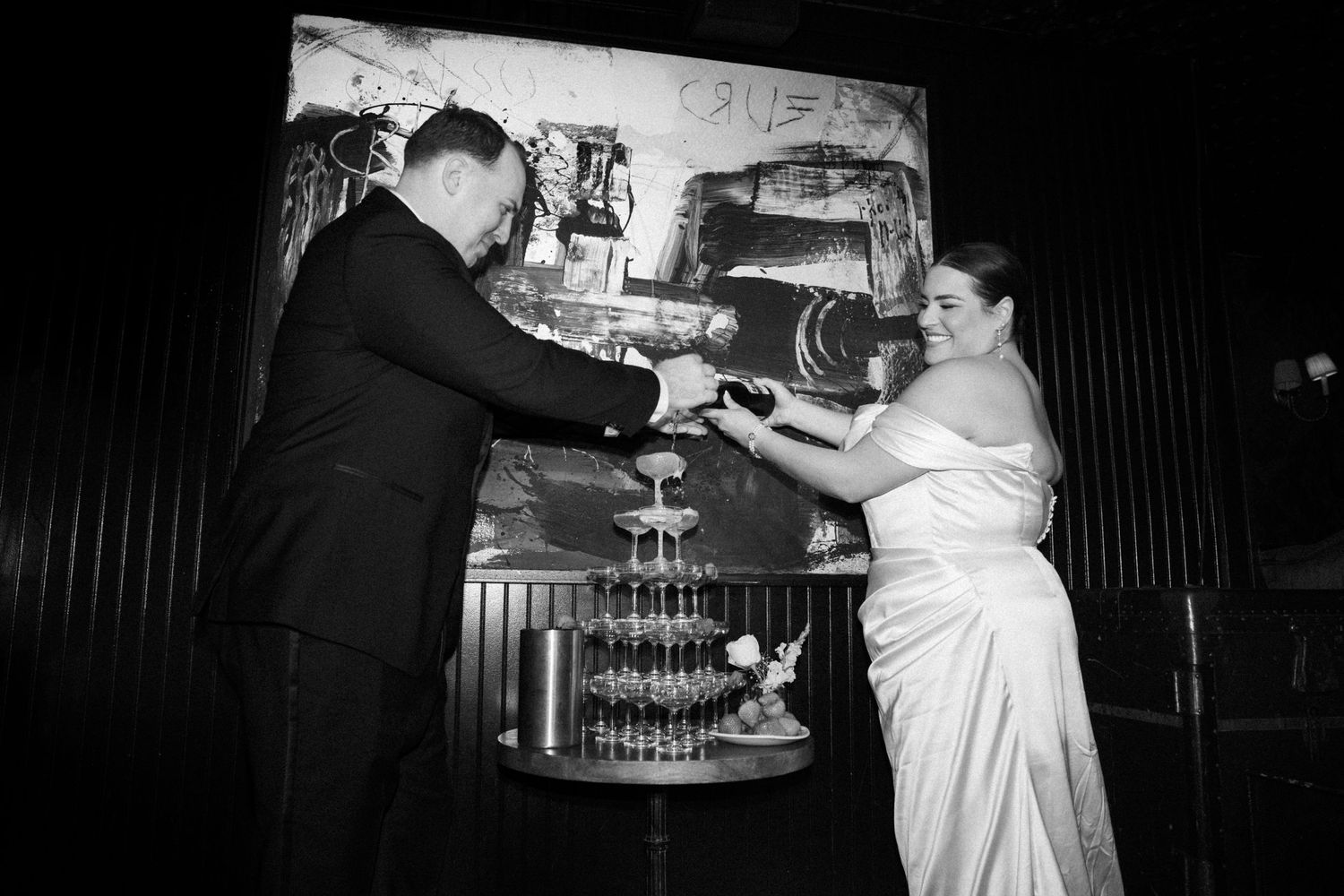 Bride and groom cutting wedding cake together in black and white photo at elegant evening reception venue.